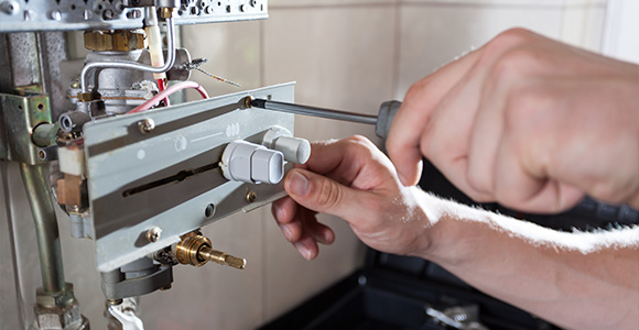 person using a screwdriver to adjust a gas valve showing plumbing work and home repair tools