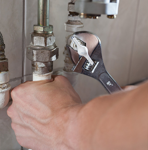 hand holding a wrench on plumbing pipes ready for repairs 6 plumbing tips for maintenance
